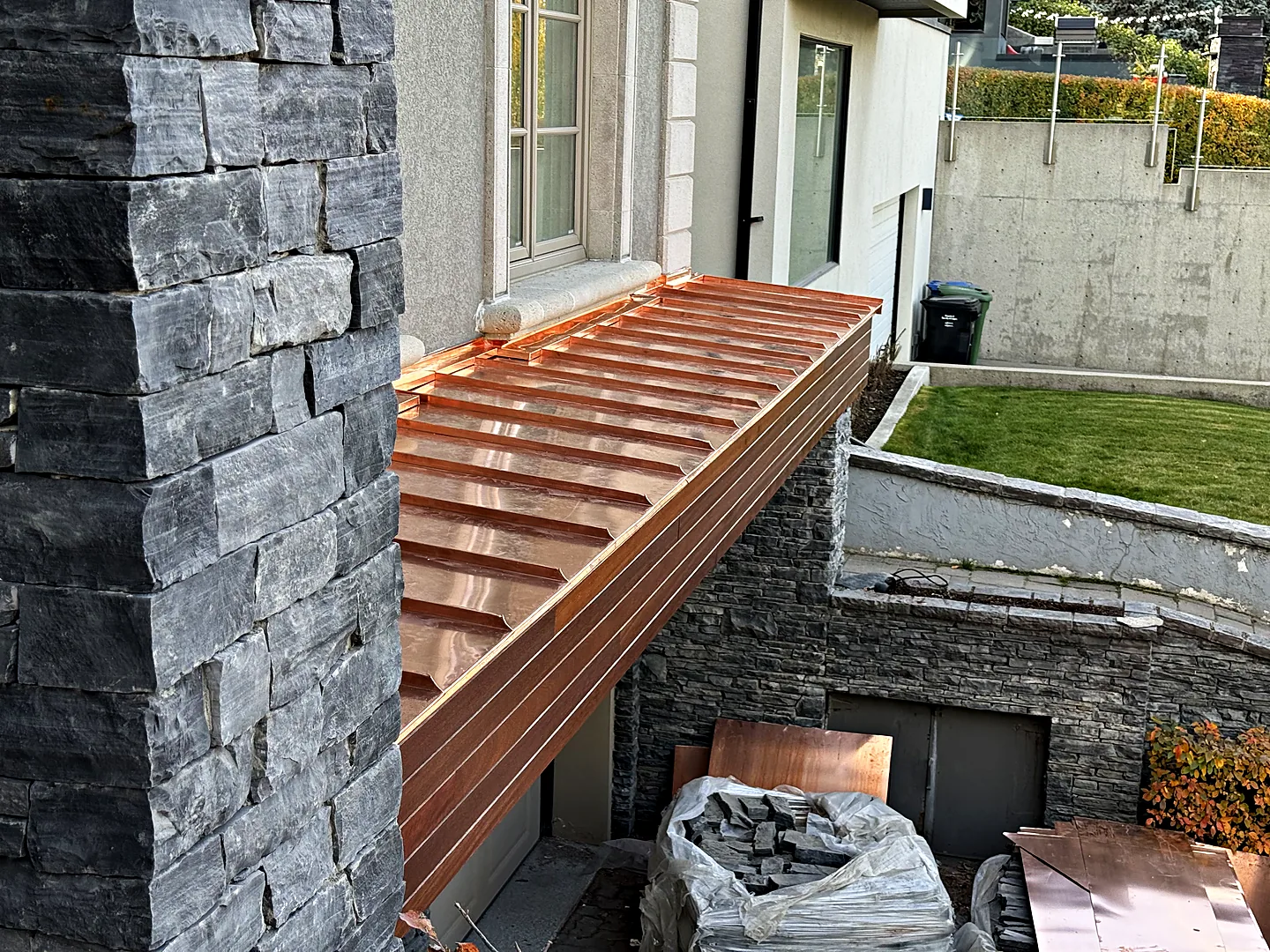 Copper canopy with standing seams beside a stone column